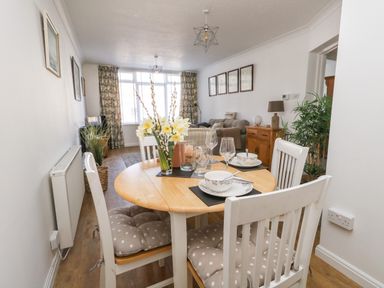 A dining table set with plates bowls glasses and cutlery beside a living room with sofa and cabinet at Beach Side in West Bay