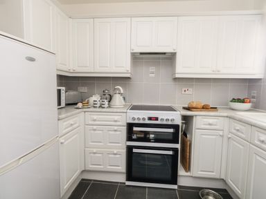 A kitchen with white cabinets a stove a refrigerator a toaster a microwave bread on a cutting board and a fruit bowl at Beach Side in West Bay