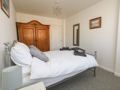 A bedroom with a metal bed frame and white bedding a wooden wardrobe a wall mirror and a small painting at Beach Side in West Bay