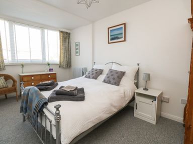 A bedroom with a metal bed frame white bedding two gray star pillows bedside table with lamp wooden chest of drawers wicker chair and framed pictures on the wall at Beach Side in West Bay