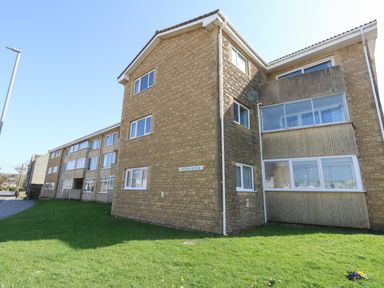 A multi-story brick apartment building with multiple windows and a grassy area in front at Beach Side in West Bay