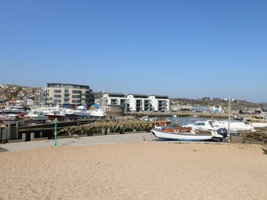 A harbor with boats docked near modern buildings and a walkway with a person walking a dog at Beach Side in West Bay