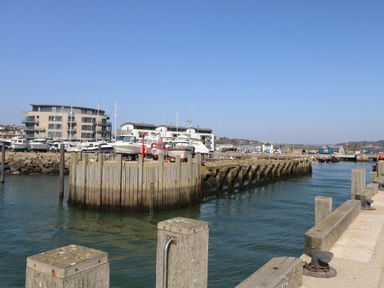 A marina with boats docked next to wooden piers and modern buildings in the background at Beach Side in West Bay