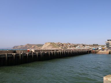 A harbor with a dock and boats near a coastal town with cliffs in the background at Beach Side in West Bay