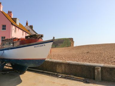A boat named Restarick on a concrete surface near a pebble beach with pink houses and a grassy cliff in the background at Beach Side in West Bay