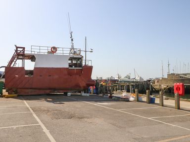 A red and white boat on dry land near a dock with other boats in the background at Beach Side in West Bay