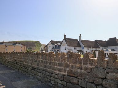 A stone wall with a thatched roof building in the background and a hill under a clear sky at Beach Side in West Bay