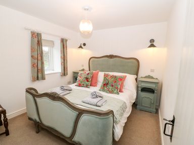 A bedroom with a double bed with pillows and blankets bedside tables and a window with curtains at Rhytty Bach in Ty Croes near Rhosneigr