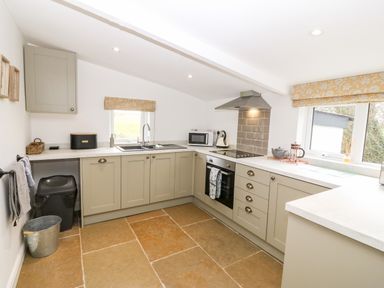 A kitchen with cabinets a stove microwave and two windows at Rhytty Bach in Ty Croes near Rhosneigr