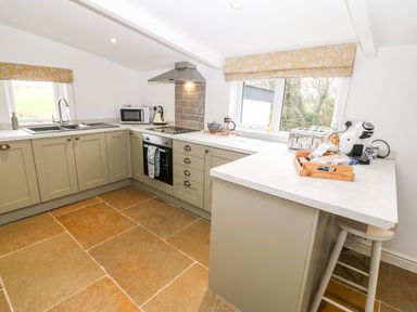 A kitchen with countertops cabinets a stove microwave toaster fen glass coffee maker and windows with patterned blinds at Rhytty Bach in Ty Croes near Rhosneigr