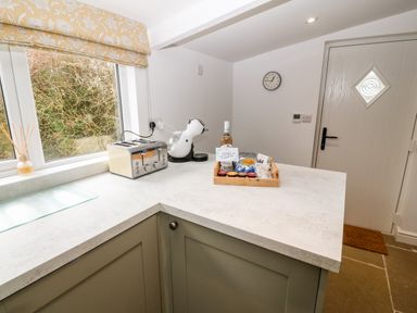 A kitchen countertop with a toaster coffee machine and a tray with snacks and a bottle near a window and door at Rhytty Bach in Ty Croes near Rhosneigr