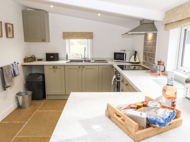 A kitchen with a wooden tray of snacks and a bottle on the counter at Rhytty Bach in Ty Croes near Rhosneigr