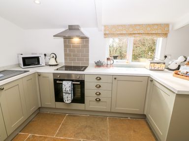 A kitchen with beige cabinets a microwave kettle oven toaster and a window at Rhytty Bach in Ty Croes near Rhosneigr