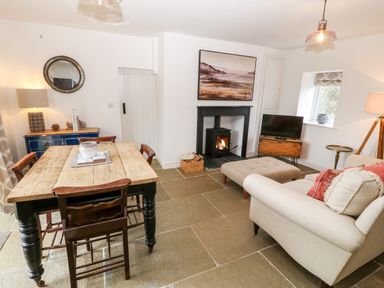 A living room with a wooden dining table and chairs a sofa and ottoman a stove fireplace a television and a blue sideboard at Rhytty Bach in Ty Croes near Rhosneigr