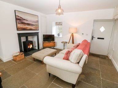 A living room with a beige sofa and ottoman a wood burning stove and a television at Rhytty Bach in Ty Croes near Rhosneigr