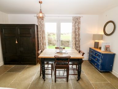A dining room with a wooden table and chairs near glass doors beside a dark cupboard and a blue dresser at Rhytty Bach in Ty Croes near Rhosneigr