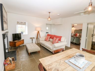 A living room with a beige sofa and ottoman wooden table small television and a floor lamp at Rhytty Bach in Ty Croes near Rhosneigr