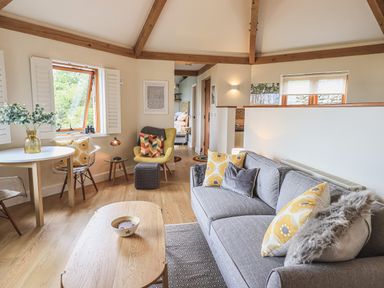 A living room with a gray sofa with yellow and gray cushions a yellow armchair a round white table with chairs a wooden coffee table and exposed wooden ceiling beams at Oversands Cottage Grange-Over-Sands