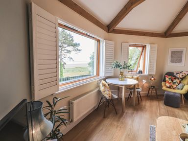 A corner dining area with a round table and two chairs near windows in a living room at Oversands Cottage in Grange-Over-Sands