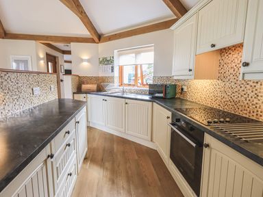 A kitchen with white cabinets black countertops a stove microwave and a window at Oversands Cottage in Grange-Over-Sands