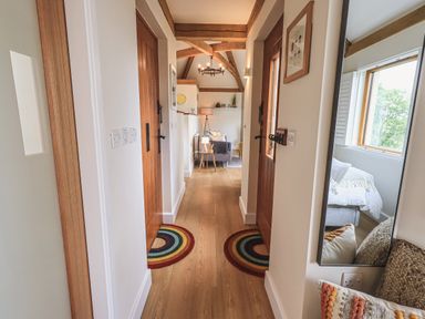 A hallway with wooden doors two round rugs and a mirror reflecting a room at Oversands Cottage in Grange-Over-Sands