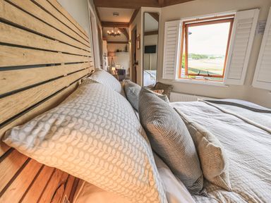 A bedroom with a wooden headboard pillows a window with open shutters and a view at Oversands Cottage in Grange-Over-Sands