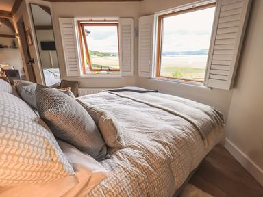 A bedroom with a bed near two windows showing a waterfront view at Oversands Cottage in Grange-Over-Sands