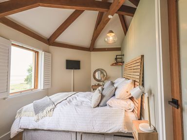 A bedroom with a bed pillows wooden headboard and exposed ceiling beams at Oversands Cottage Grange-Over-Sands