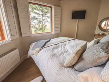 A bedroom with a bed near windows and a TV on the wall at Oversands Cottage in Grange-Over-Sands