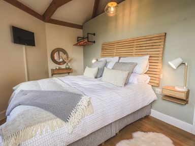 A bedroom with a bed with pillows and blankets a wall lamp a round mirror and a small shelf at Oversands Cottage in Grange-Over-Sands