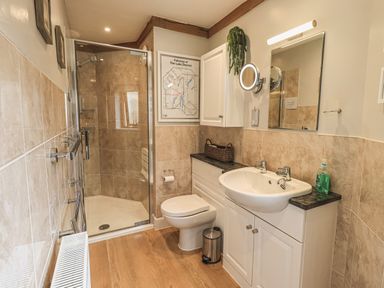 A bathroom with a shower enclosure a toilet a sink with cabinets a mirror and a radiator at Oversands Cottage Grange-Over-Sands