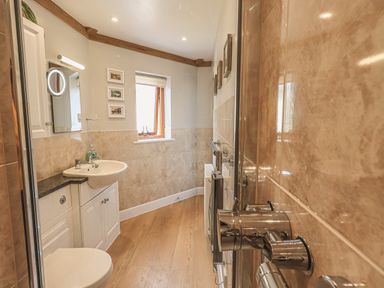 A bathroom with a sink, toilet, glass shower door, and window at Oversands Cottage in Grange-Over-Sands
