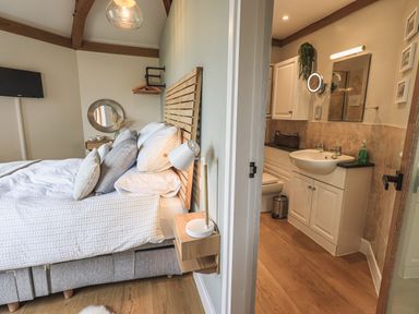 A bedroom with a bed and bedside lamp next to a bathroom with a sink and mirror at Oversands Cottage in Grange-Over-Sands