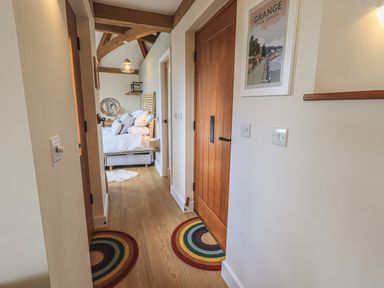 A hallway with wooden doors and two round rainbow rugs leading to a bedroom with a bed and pillows at Oversands Cottage in Grange-Over-Sands