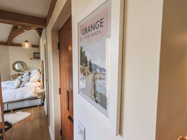 A hallway leading to a bedroom with a wooden door and a framed picture of Grange Over-Sands on the wall at Oversands Cottage in Grange-Over-Sands