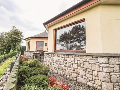 An exterior view of a building with stone and plaster walls outdoor table and chairs and plants along a fence at Oversands Cottage in Grange-Over-Sands