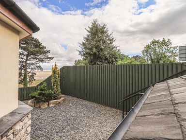 A fenced gravel yard with small trees and a stone border near a house at Oversands Cottage in Grange-Over-Sands