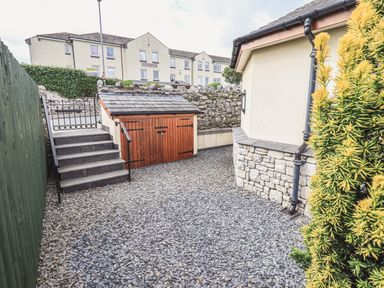 A gravel yard with steps leading to a gate and a wooden storage shed next to a house at Oversands Cottage in Grange-Over-Sands