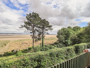 A coastal landscape with trees bushes and a sandy beach visible beyond at Oversands Cottage in Grange-Over-Sands