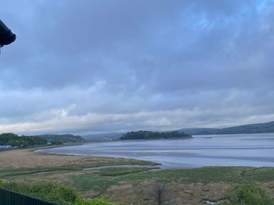 A coastal landscape with water, grassy marshland, and distant hills under a cloudy sky at Oversands Cottage in Grange-Over-Sands