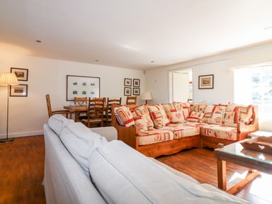 A living room with a patterned wooden sofa a grey fabric sofa a dining table with wooden chairs and framed pictures on walls at 1 The Lane in Chipping Norton