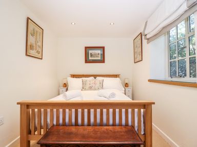 A bedroom with a wooden bed frame two bedside tables with lamps framed artwork on walls and a window at 1 The Lane in Chipping Norton