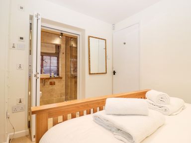 A bedroom with a wooden bed frame white towels on the bed and a bathroom with tiled walls visible through an open door at 1 The Lane in Chipping Norton