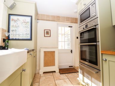 A kitchen with green cabinets a double oven a sink a door and framed pictures at 1 The Lane in Chipping Norton