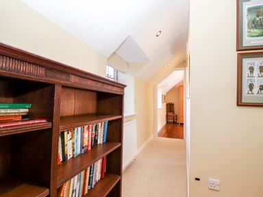 A hallway with a wooden bookshelf filled with books and a chair visible at the end at 1 The Lane in Chipping Norton