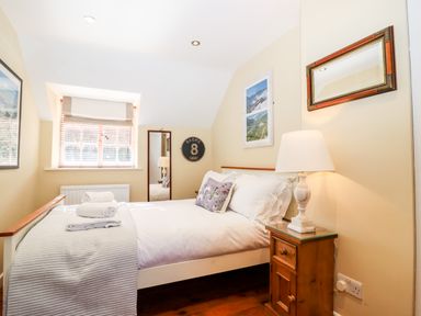 A bedroom with a bed, bedside table with lamp, window with blinds, and wall decorations at 1 The Lane in Chipping Norton