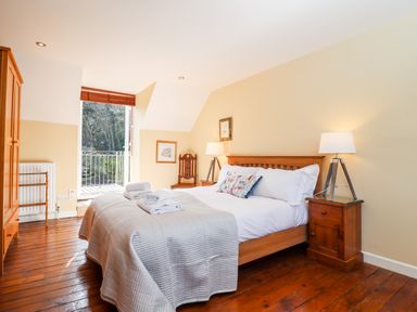 A bedroom with a wooden bed and bedside tables with lamps a wardrobe a chair and an open door leading outside at 1 The Lane in Chipping Norton