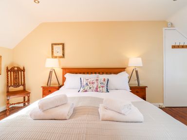 A bedroom with a wooden bed framed by two bedside tables with lamps and a carved wooden chair at 1 The Lane in Chipping Norton