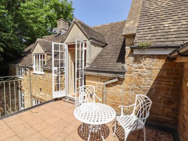 A terrace with white metal table and chairs next to a stone house with open French doors at 1 The Lane in Chipping Norton