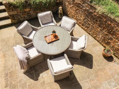 An outdoor patio area with a round glass table surrounded by six cushioned wicker chairs at 1 The Lane in Chipping Norton